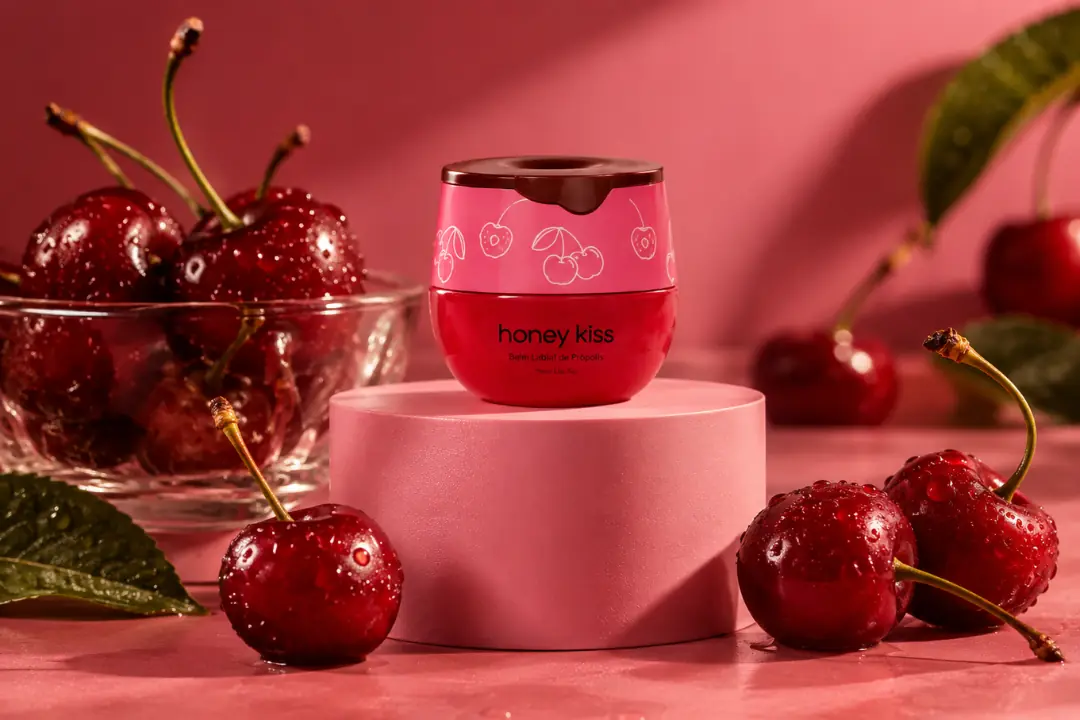Pote do balm labial HoneyKiss sabor Cereja, cercado de cerejas