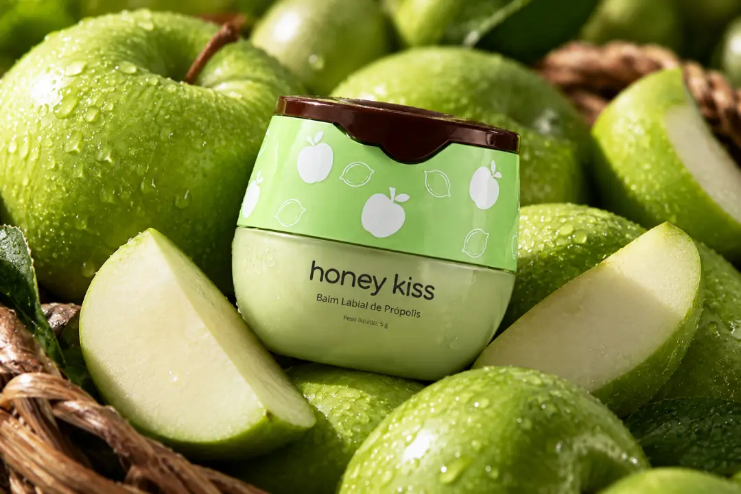Pote do balm labial HoneyKiss sabor Maçã Verde, sobre mesa com maçãs, foto 4